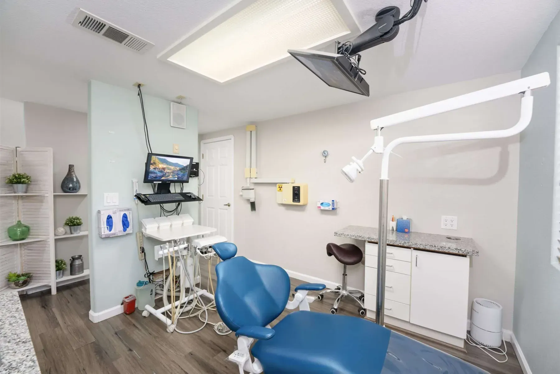 A bright treatment room with a blue dental chair and open shelving